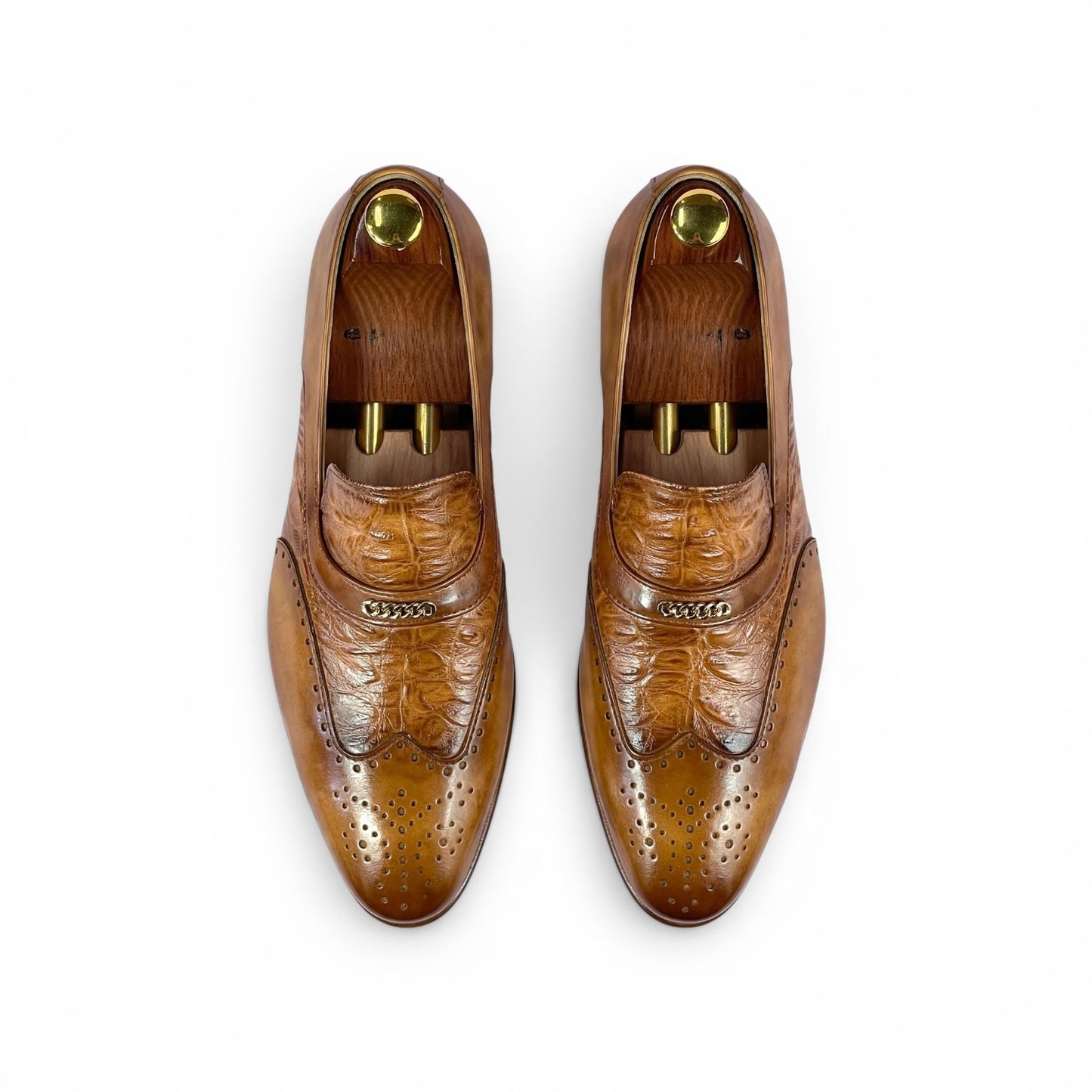 A pair of men's brown leather loafers with brogue detailing, shown from a top-down view on white shoe trees against a white background.