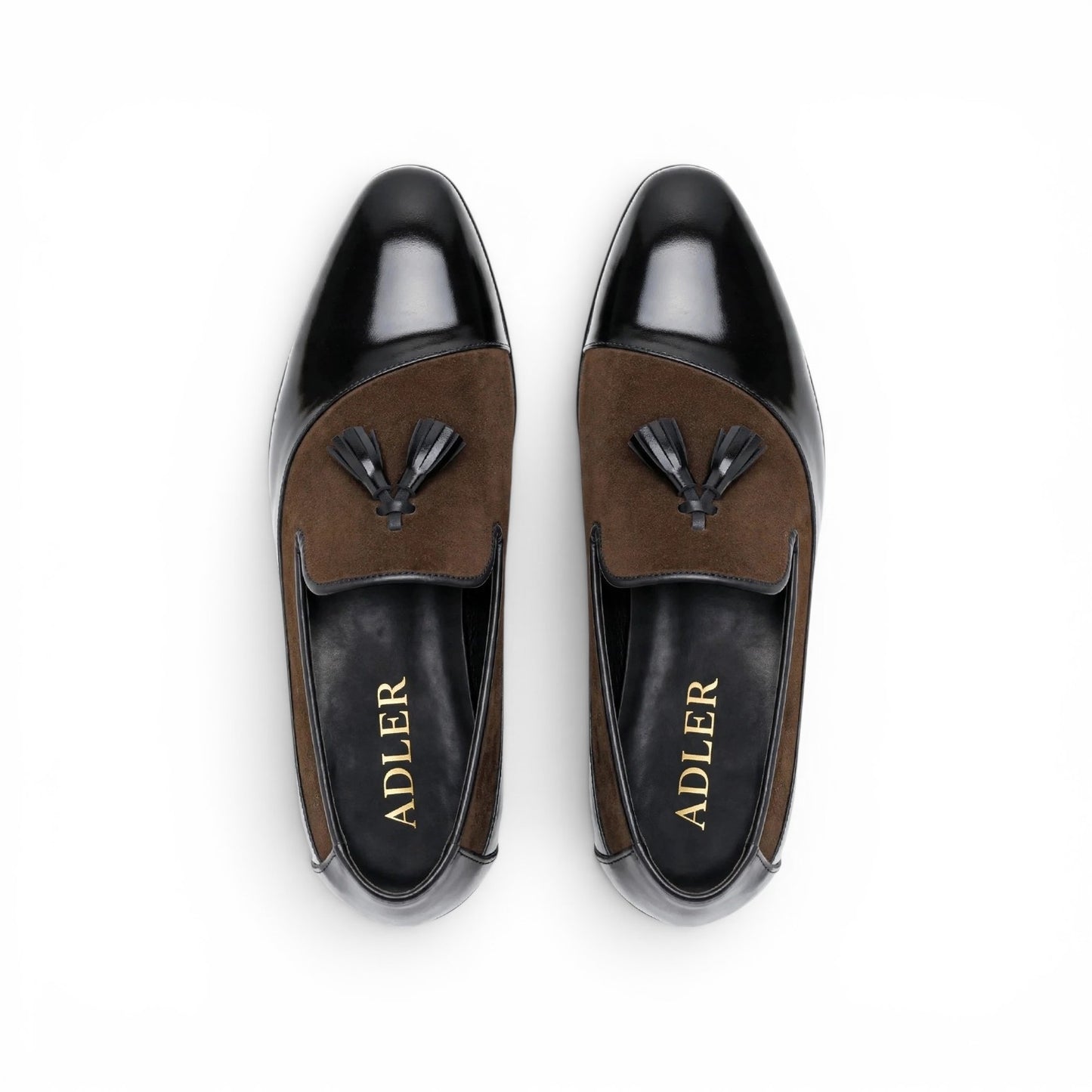 A pair of men's loafers shown from a top-down view on a white background. The shoes feature a glossy black leather toe cap and heel counter, a brown suede vamp with a black tassel, and a black insole with the brand name 'ADLER' in gold lettering.