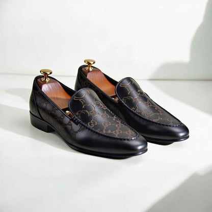 Pair of black loafers with gold accents on a white surface