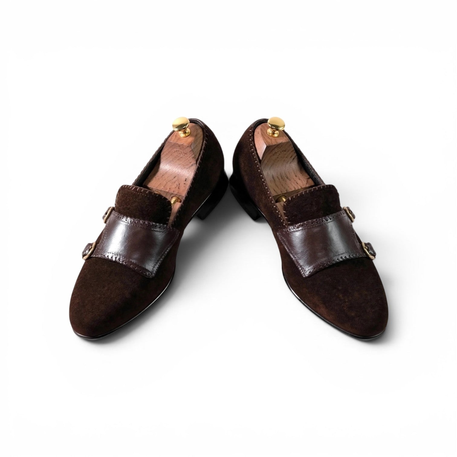 A pair of dark brown suede and leather loafers displayed on wooden shoe trees against a clean white background.