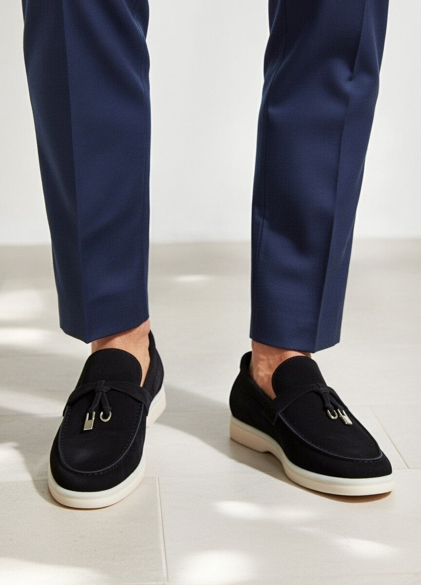 Black loafers worn with navy pants on a white background