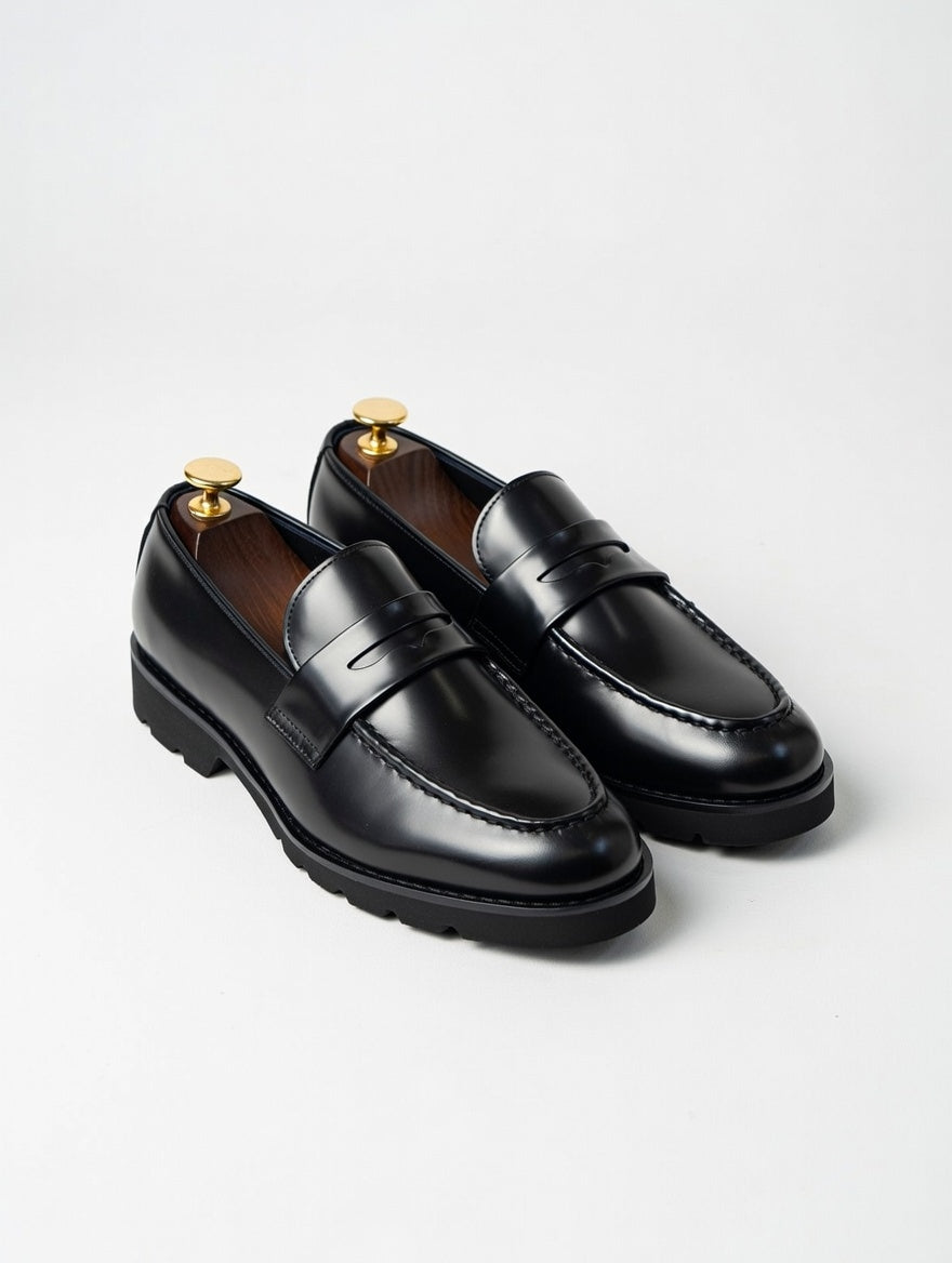 Pair of black loafers with gold accents on a light gray background