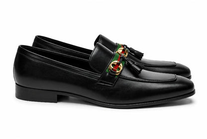 A pair of black leather tassel loafers with the signature Gucci green and red web stripe and gold-tone GG logo on the vamp, shown against a plain white background.