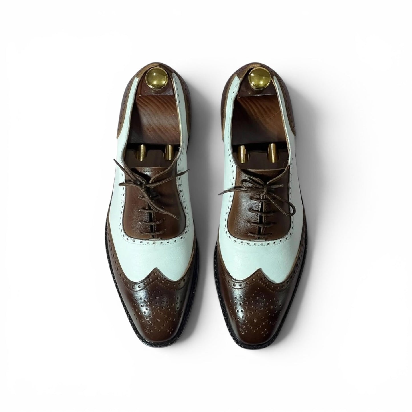 A pair of men's wingtip oxford shoes in a two-tone brown and pale mint green colorway, displayed on wooden shoe trees against a clean white background.