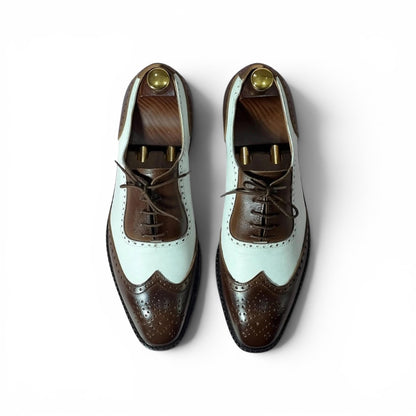 A pair of men's wingtip oxford shoes in a two-tone brown and pale mint green colorway, displayed on wooden shoe trees against a clean white background.