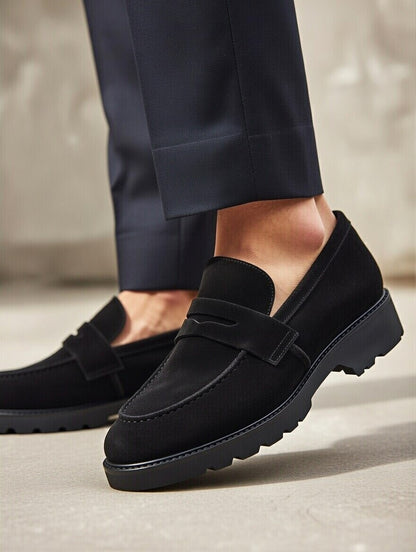 Black loafers worn with navy pants on a neutral background