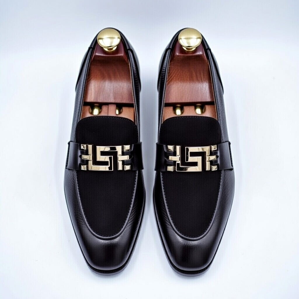 Black loafers with gold accents on a white background