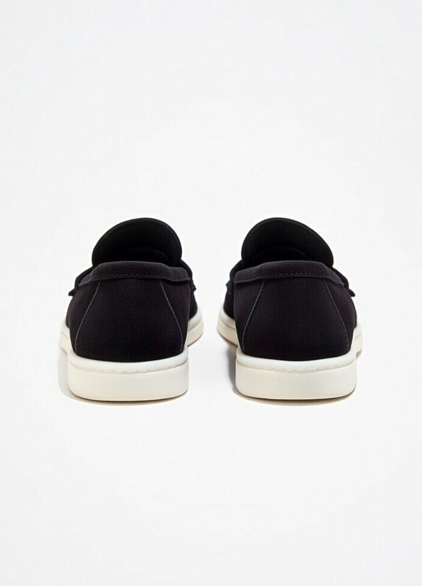 Black slip-on shoes with white soles on a light gray background