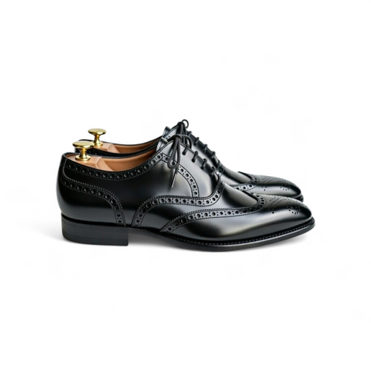 Pair of black dress shoes with brogue detailing on a white background