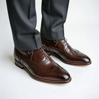 Brown dress shoes with wingtip design worn with gray pants on a light background