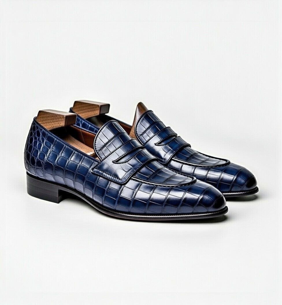 Pair of blue crocodile-patterned loafers on a light gray background