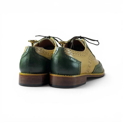 A pair of men's wingtip oxford shoes shown from the back, featuring dark green and tan leather panels, black laces, and dark brown stacked soles on a white background.