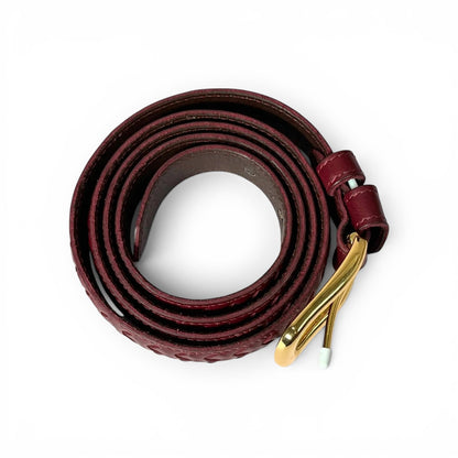 A dark burgundy leather belt coiled on a white background, featuring a textured pattern and a polished gold-tone metal buckle.