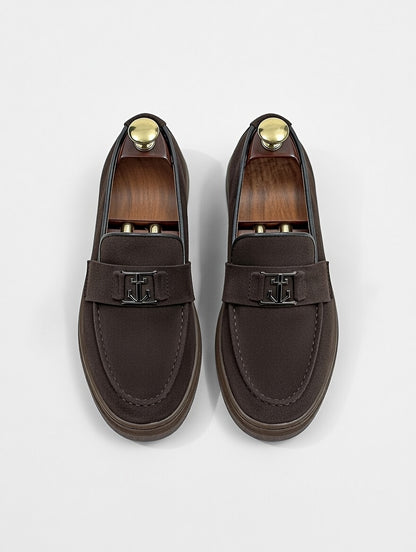 Pair of brown loafers with gold accents on a light gray background