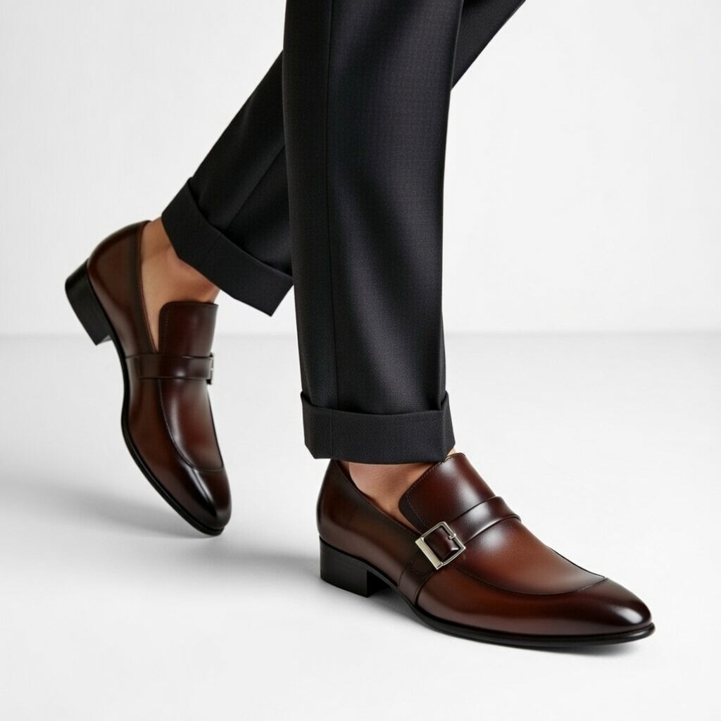 Brown dress shoes with a buckle worn with black pants on a light gray background