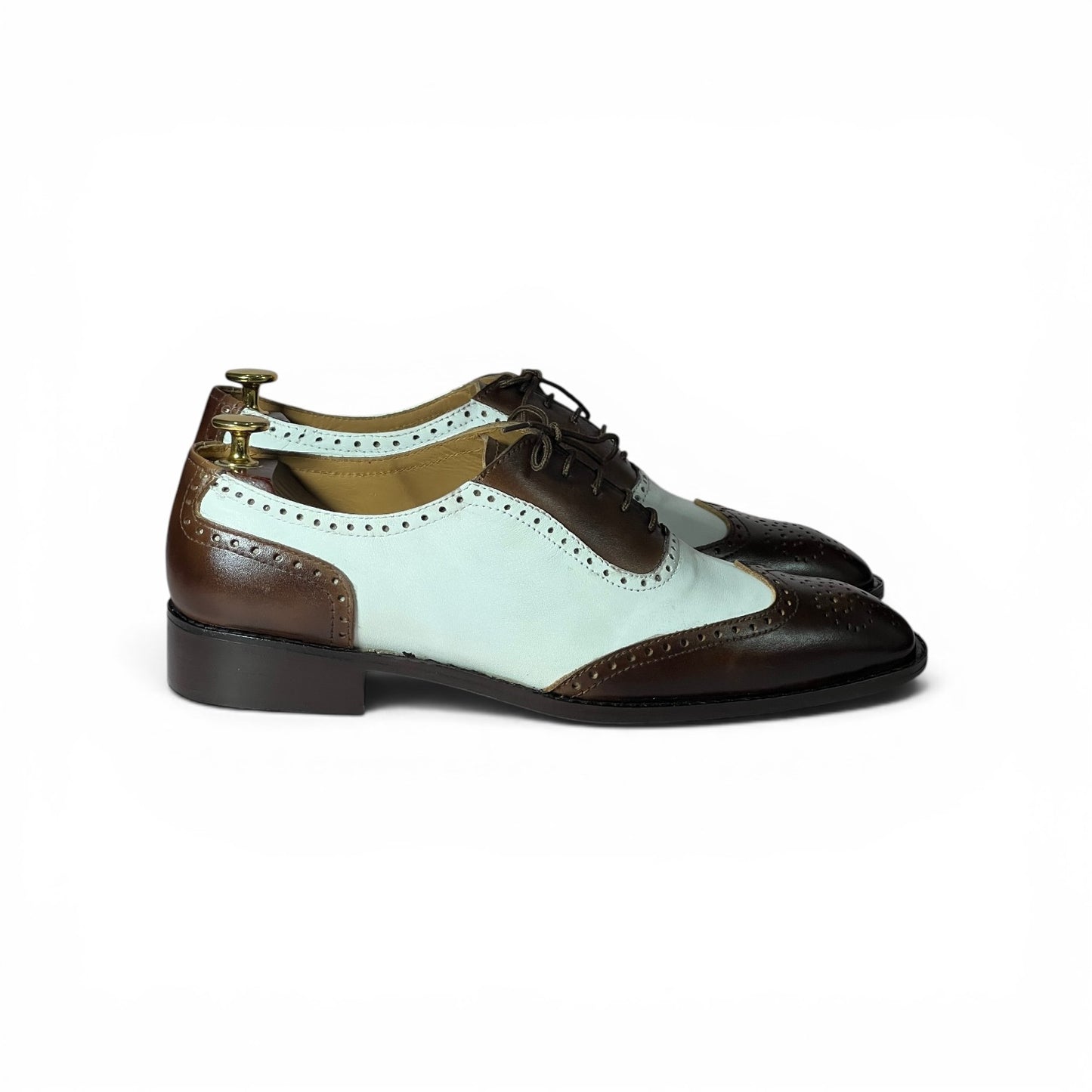A pair of men's wingtip oxford shoes featuring a color-blocked design with dark brown leather, a pale mint green leather panel, and black laces, shown from a side profile on a white.background.