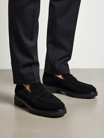 Black loafers worn with black pants on a light gray background