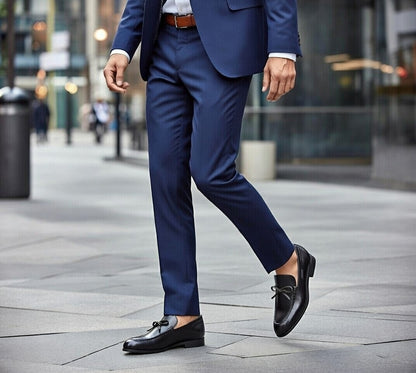 Person wearing a blue suit and black loafers on a city street.