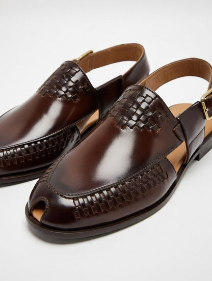 Pair of brown leather sandals with woven detailing on a light gray background