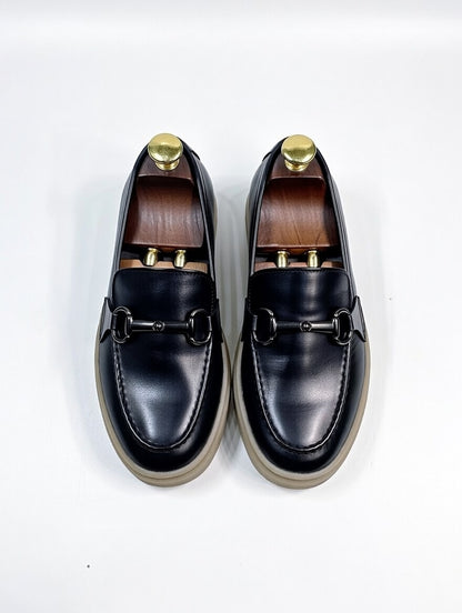 Pair of black loafers with gold accents on a white background