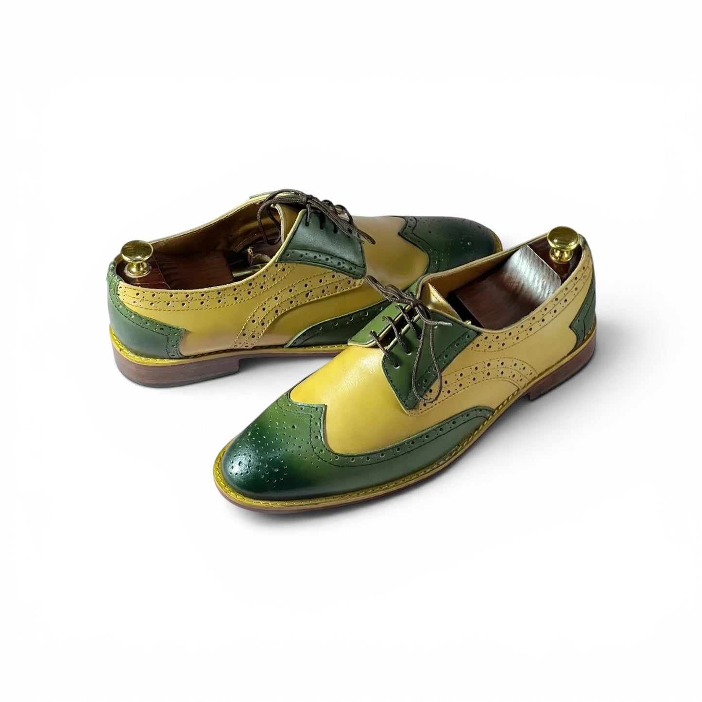 A pair of men's wingtip oxford shoes with a distinctive two-tone color-blocked design in olive green and mustard yellow, shown on a clean white background.
