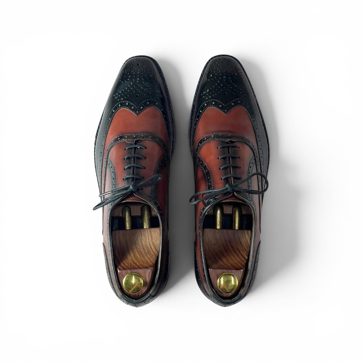 A pair of men's wingtip oxford shoes shown from a top-down view on a white background. The shoes feature a two-tone color-blocked design with a dark navy blue wingtip and toe section, and a reddish-brown leather vamp and quarter section.