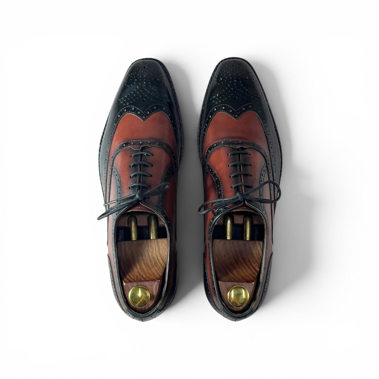 A pair of men's wingtip oxford shoes shown from a top-down view on a white background. The shoes feature a two-tone color-blocked design with a dark navy blue wingtip and toe section, and a reddish-brown leather vamp and quarter section.
