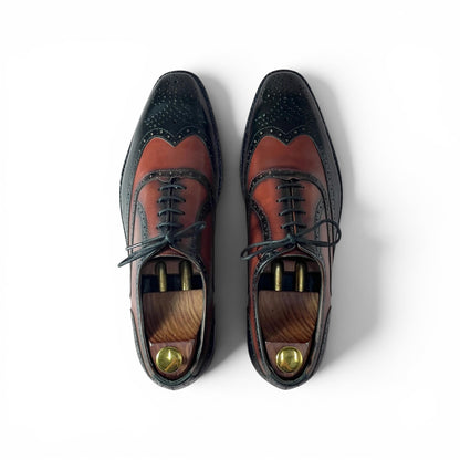 A pair of men's wingtip oxford shoes shown from a top-down view on a white background. The shoes feature a two-tone color-blocked design with a dark navy blue wingtip and toe section, and a reddish-brown leather vamp and quarter section.