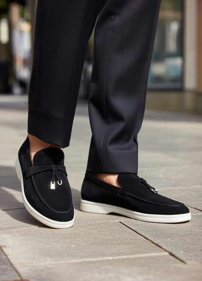 Black loafers worn with dark trousers on a pavement.