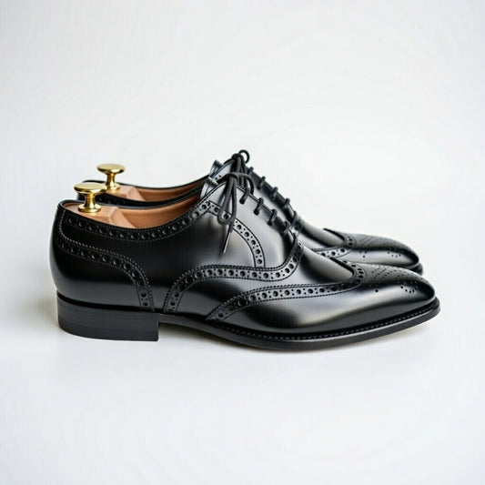 Black dress shoes with brogue detailing on a light gray background