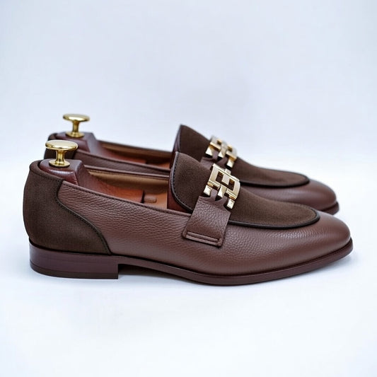 Brown leather loafers with gold buckles on a light gray background