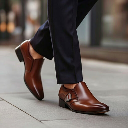 Brown leather shoes with a silver buckle worn with dark pants on a blurred background