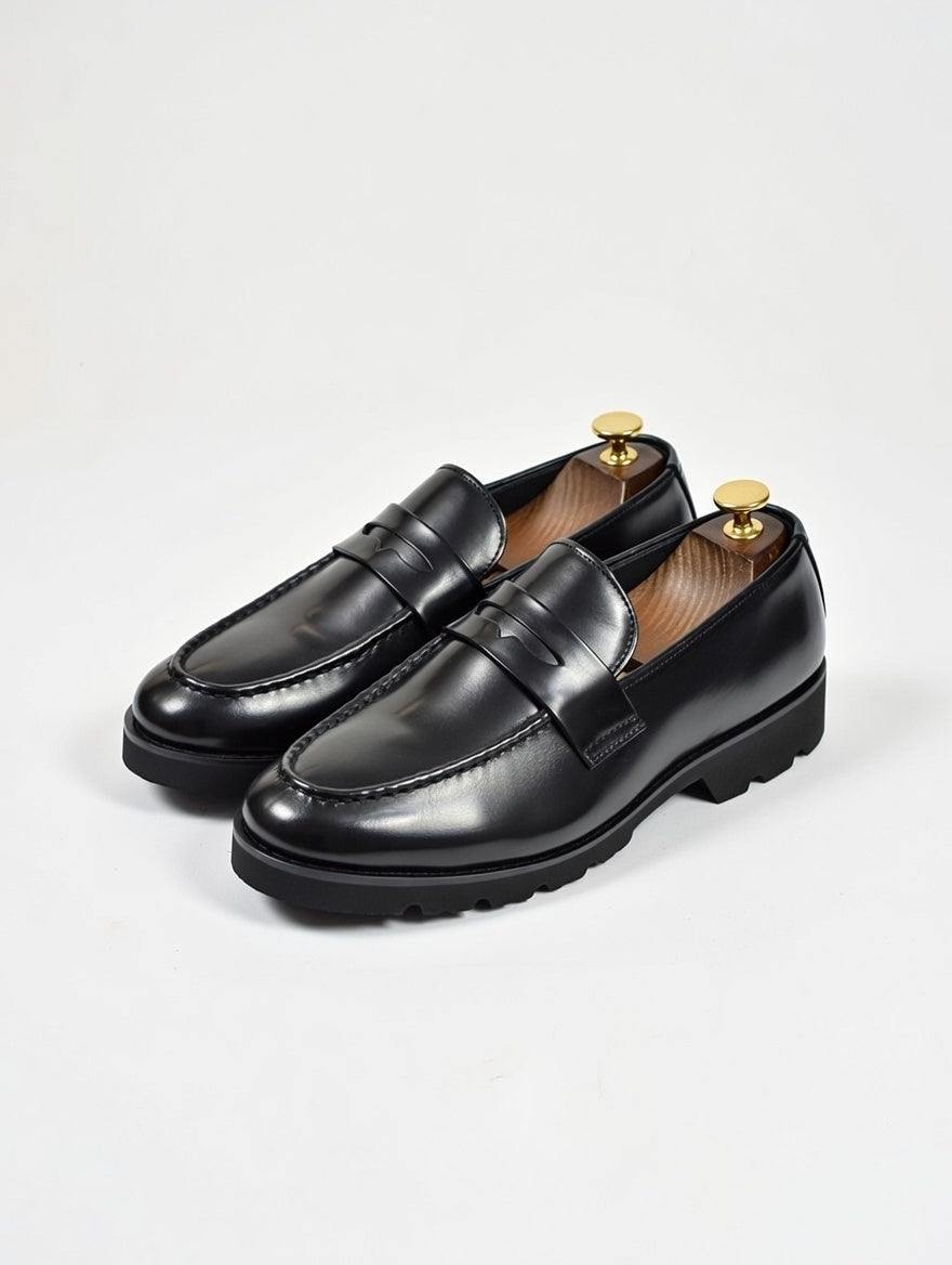 Pair of black loafers with gold accents on a light gray background
