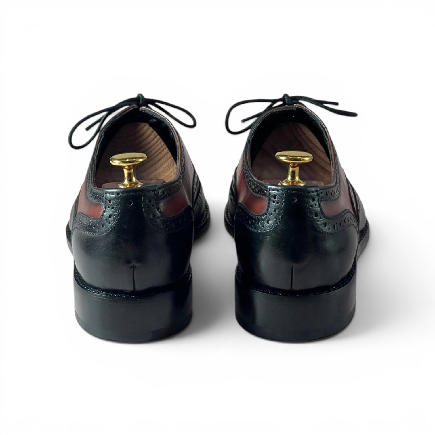 A pair of black leather wingtip oxford shoes shown from the back, with gold shoe tree inserts in the heels, on a clean white background.