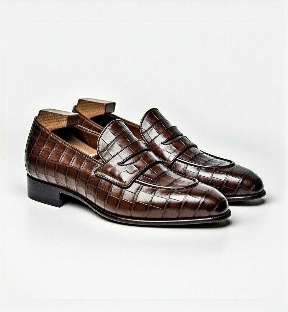 Pair of brown crocodile-patterned loafers on a light gray background