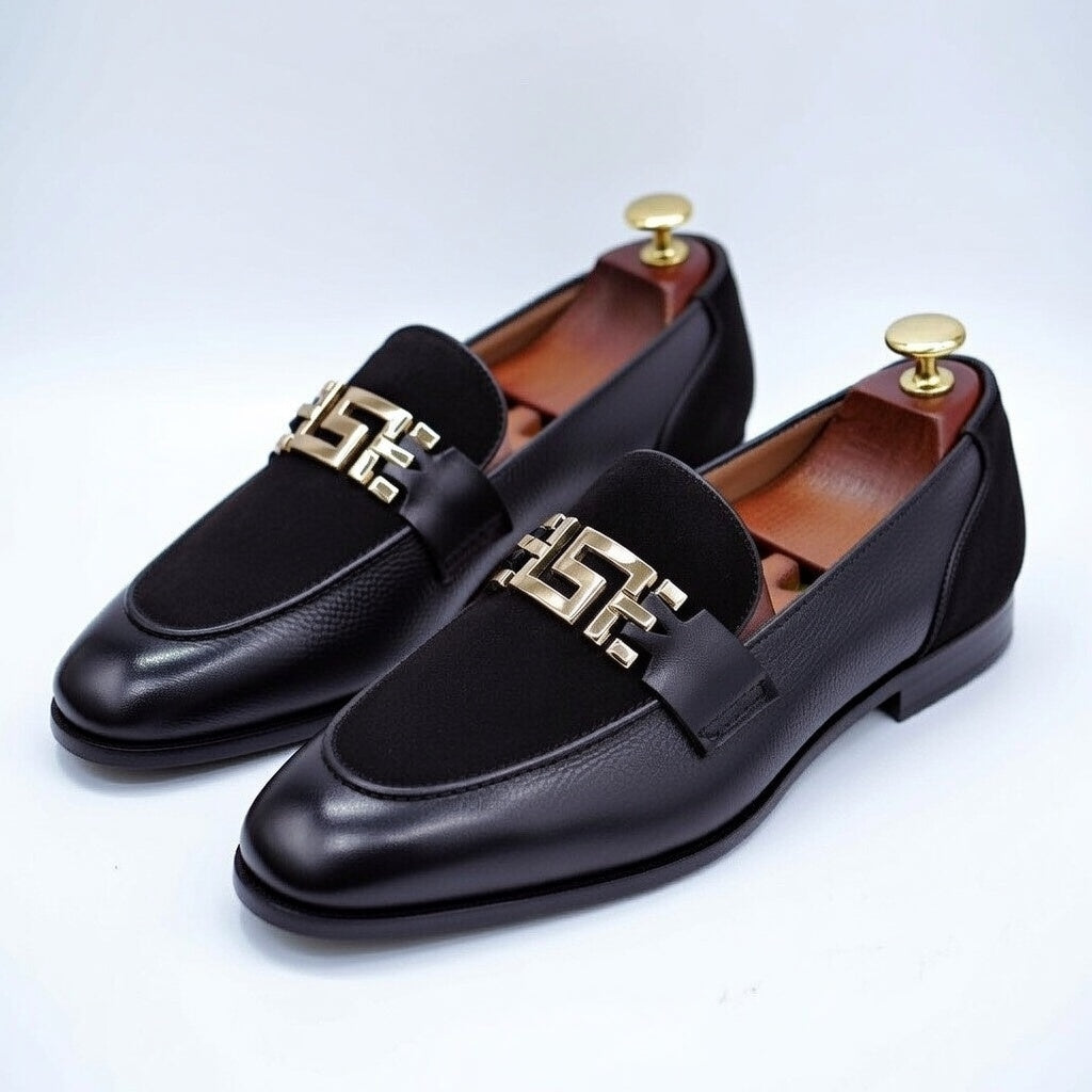 Pair of black loafers with gold accents on a light gray background