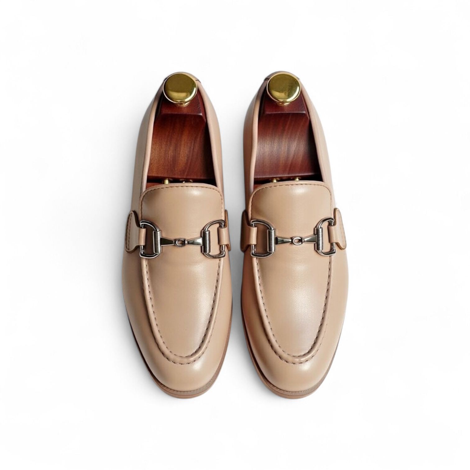 Pair of beige loafers with metallic buckles on a white background