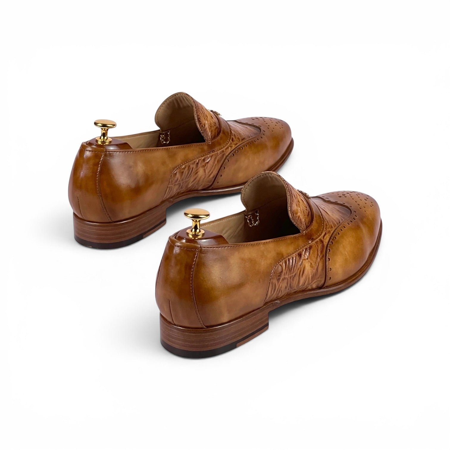 A pair of men's brown leather loafers with brogue detailing and decorative stitching, shown on shoe trees against a plain white background.