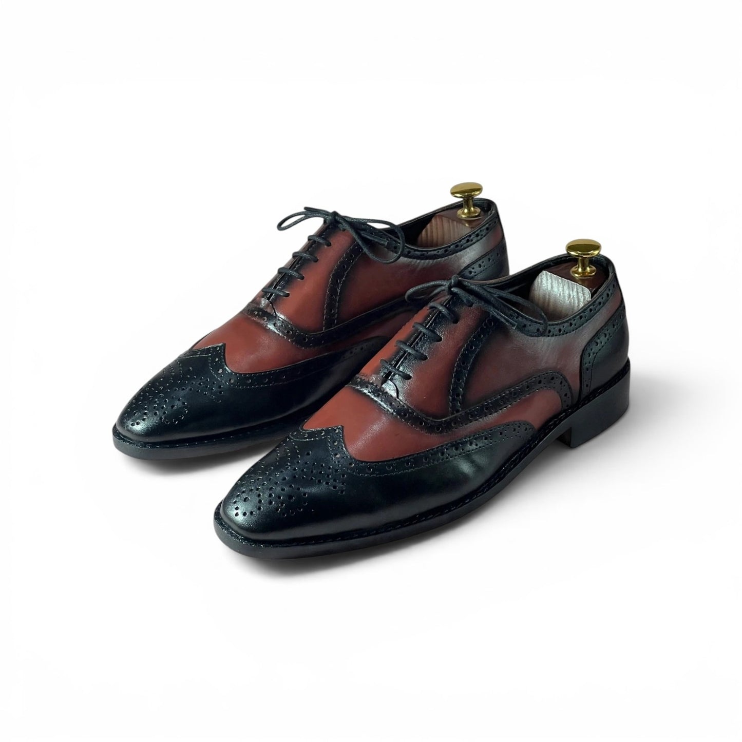 A pair of men's wingtip oxford shoes in a two-tone brown and black leather design, displayed on white shoe trees against a clean white background.