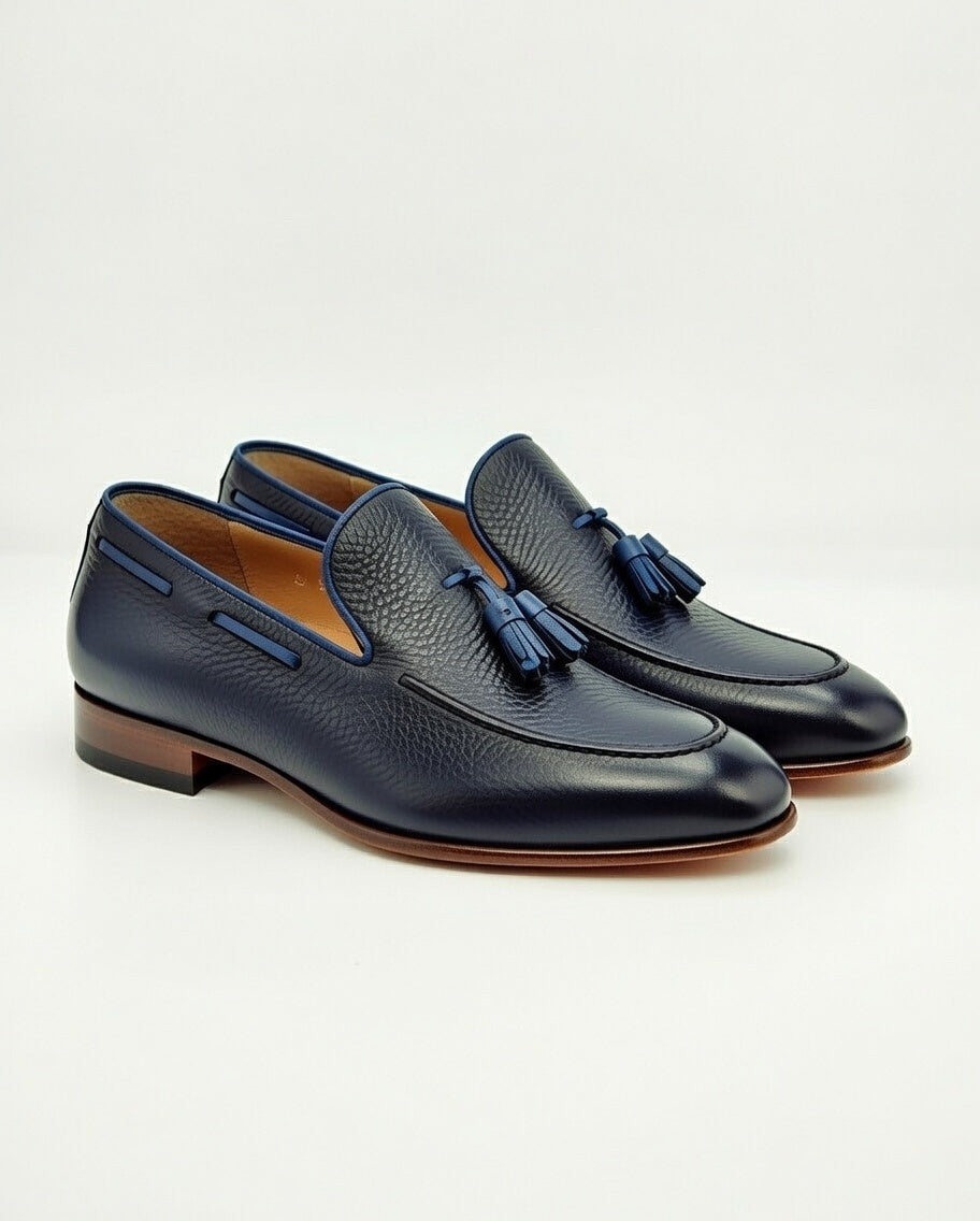 Pair of navy blue loafers with tassels on a light gray background