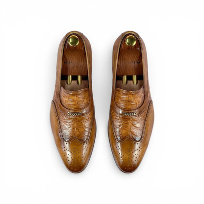 A pair of men's brown leather loafers with brogue detailing, shown from a top-down view on white shoe trees against a white background.