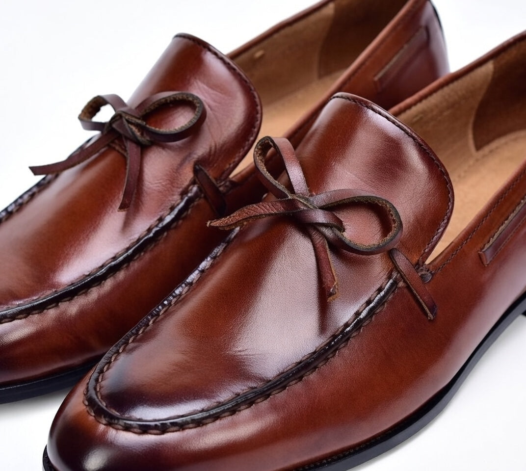 Brown leather loafers with braided laces on a white background