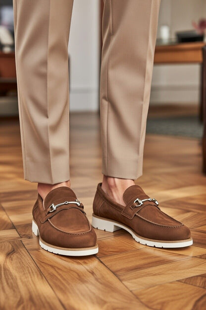 Brown loafers worn with beige pants on a wooden floor.