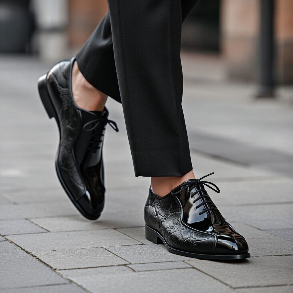 Black leather shoes worn with black pants on a pavement.