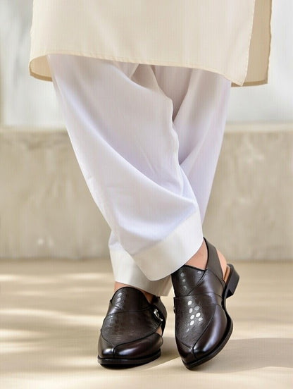 Brown leather shoes worn with white pants on a neutral background