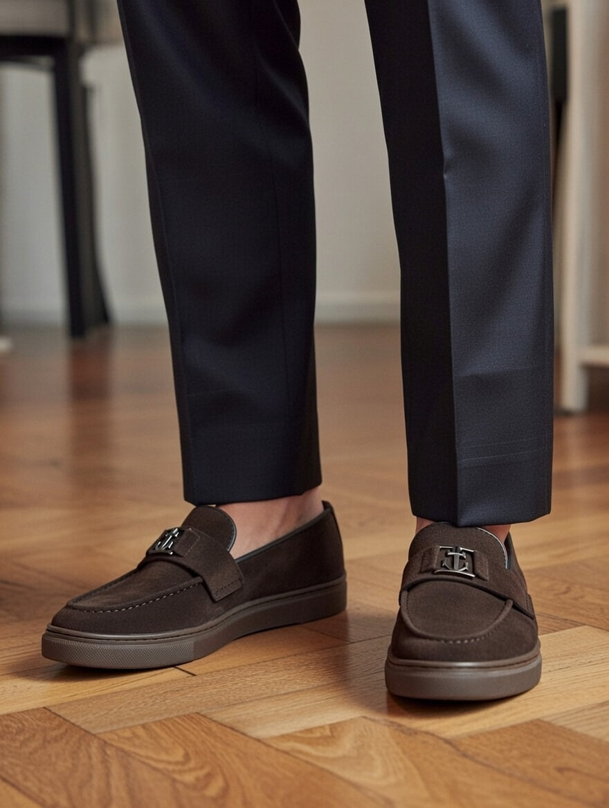 Brown loafers worn with dark pants on a wooden floor