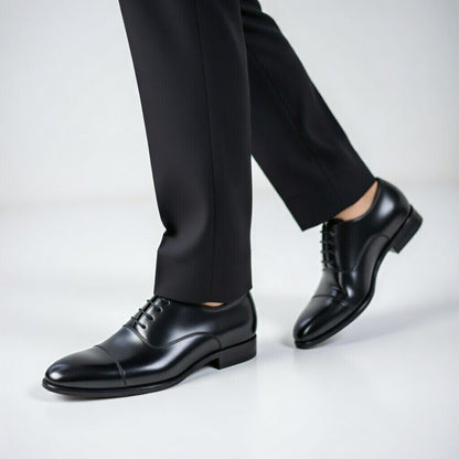 Black dress shoes worn with black pants on a light gray background