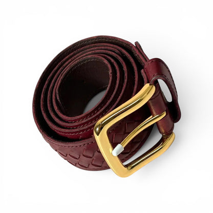 A dark burgundy woven leather belt with a polished gold buckle, coiled on a clean white background.