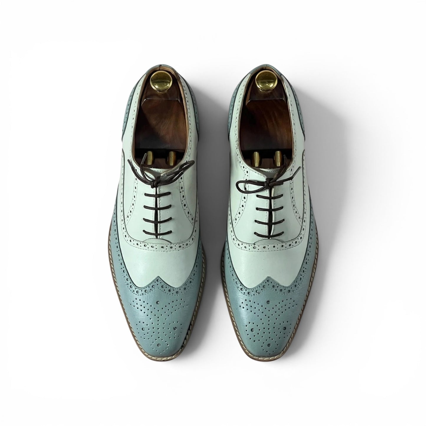 A pair of men's wingtip oxford shoes in a two-tone pale mint green and dusty blue colorway, featuring black laces and decorative perforations, shown from a top-down view on a white background.