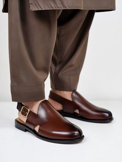 Brown leather shoes worn with brown pants on a light gray background